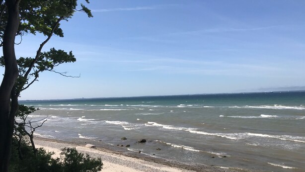 Uma praia com ondas, céu claro e terra ao longe.