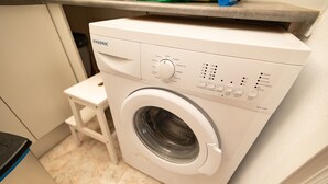 A front-loading washing machine with a control panel, a small stool, and a tiled floor. - Luxurious apartment with garden (Agaete)
