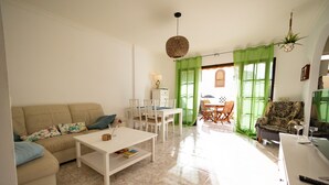 A living room with a beige sofa, white coffee table, and a dining area with a table and chairs. - Luxurious apartment with garden (Agaete)