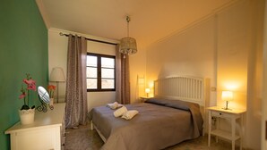 A bedroom with a bed, bedside lamps, a dresser, a window with curtains, and a hanging light fixture. - Luxurious apartment with garden (Agaete)