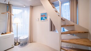 A modern hotel room with a wooden staircase, a bedside table with a lamp, a small round table, and a window with curtains. - The Phase Boutique Hotel (Seoul)