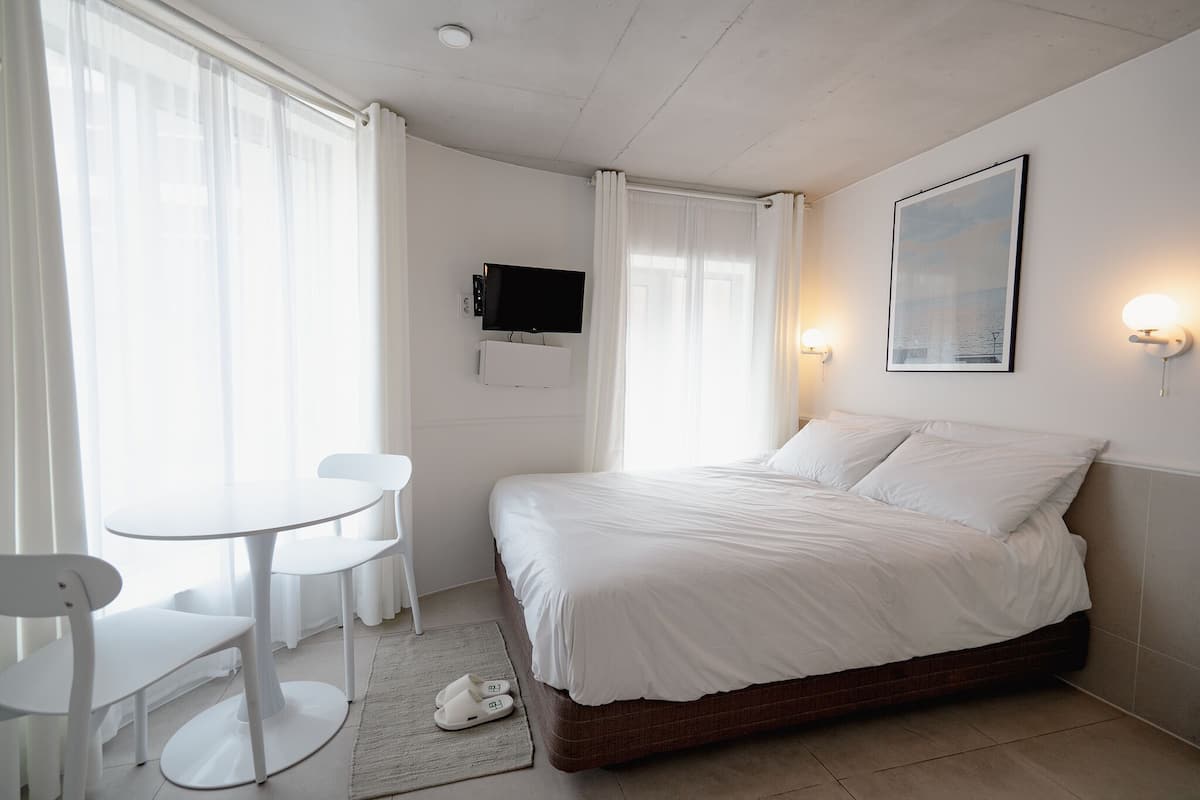 A bedroom with a bed, a TV mounted on the wall, and a small table with chairs.