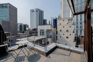 A rooftop terrace with a table and chairs, surrounded by a metal railing, overlooking a cityscape with modern buildings. - The Phase Boutique Hotel (Seoul)