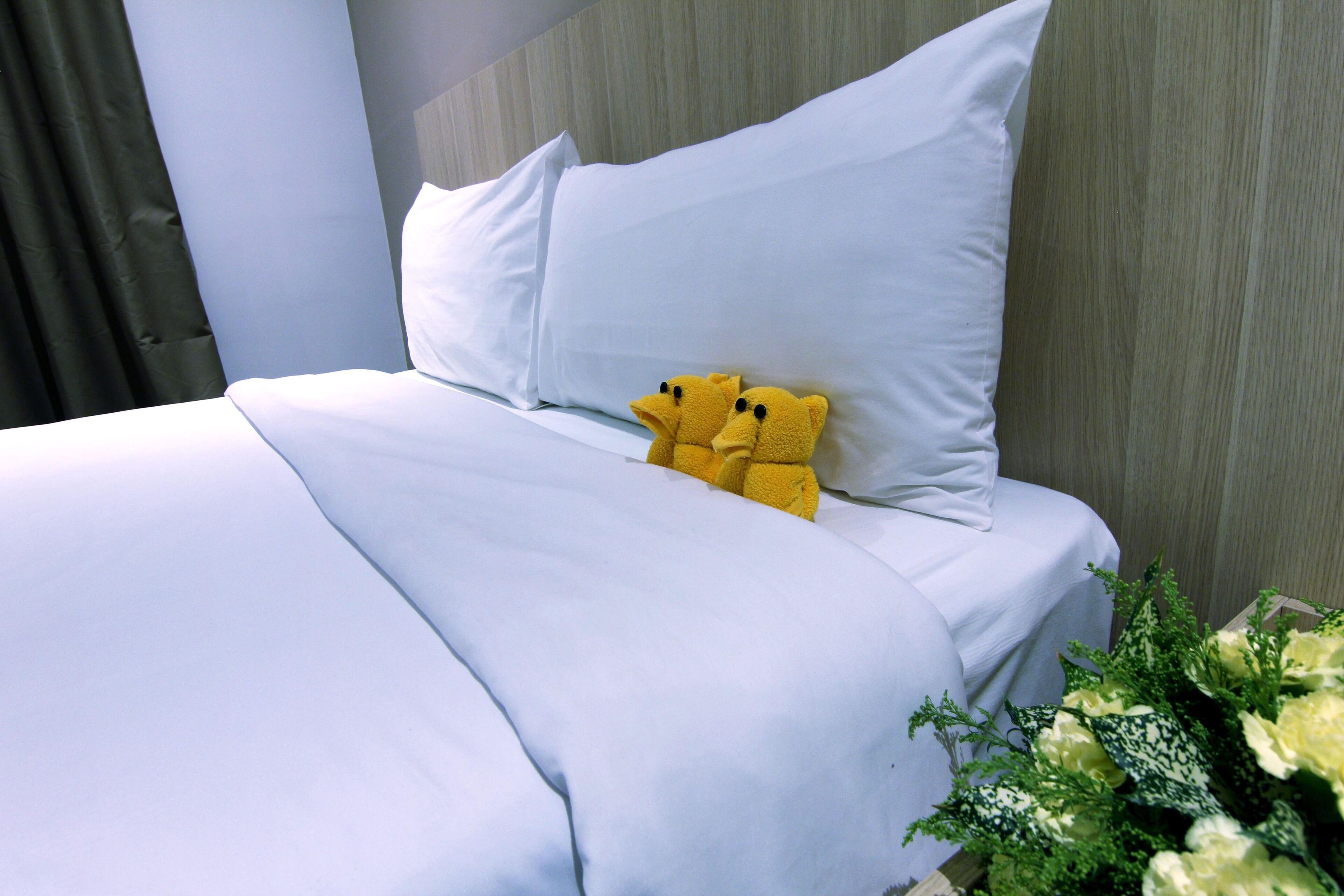 A neatly made bed with white linens and two plush yellow teddy bears placed on the pillows.