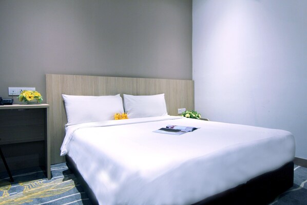 A neatly made bed with white linens, a wooden headboard, and a small bedside table with a lamp and a flower arrangement.