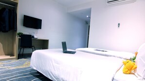 Una camera d'albergo con due letti, una scrivania con un portatile, una TV a parete e un armadio con abiti appesi.