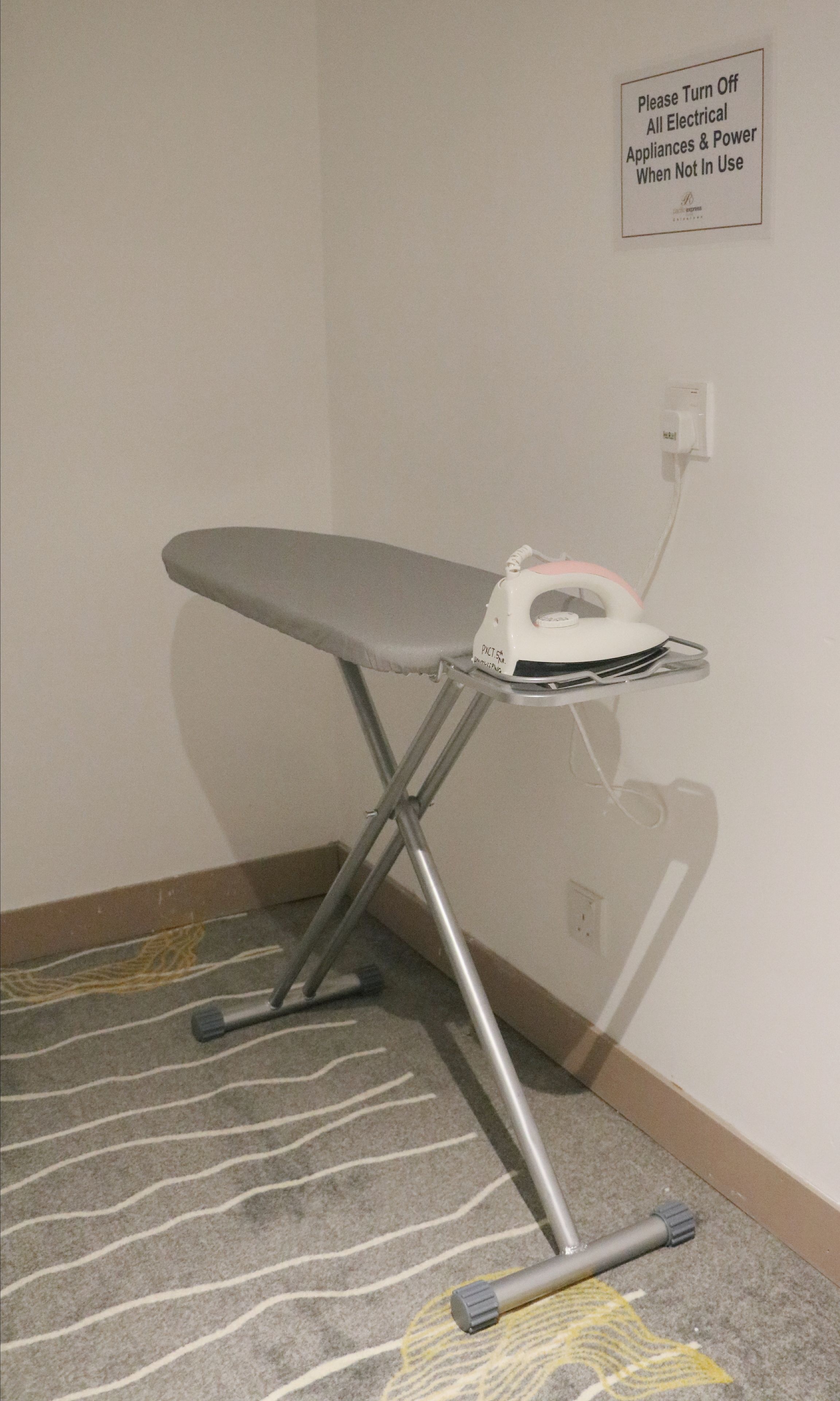 Ein Bügeleisenbrett mit Bügeleisen und einem Schild, das darauf hinweist, elektrische Geräte nicht in Gebrauch auszuschalten.