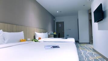 A hotel room with two beds, a flat-screen TV mounted on the wall, a desk with a laptop, and a patterned carpet.