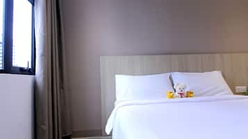 A hotel room with a bed, a window with curtains, and a teddy bear on the bed.
