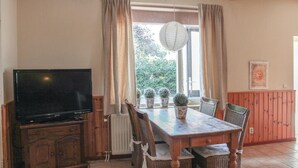 A dining area with a wooden table, chairs, a television, and potted plants.