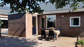 A brick building with a patio area featuring a table and chairs, a blue door, and a window with a view.