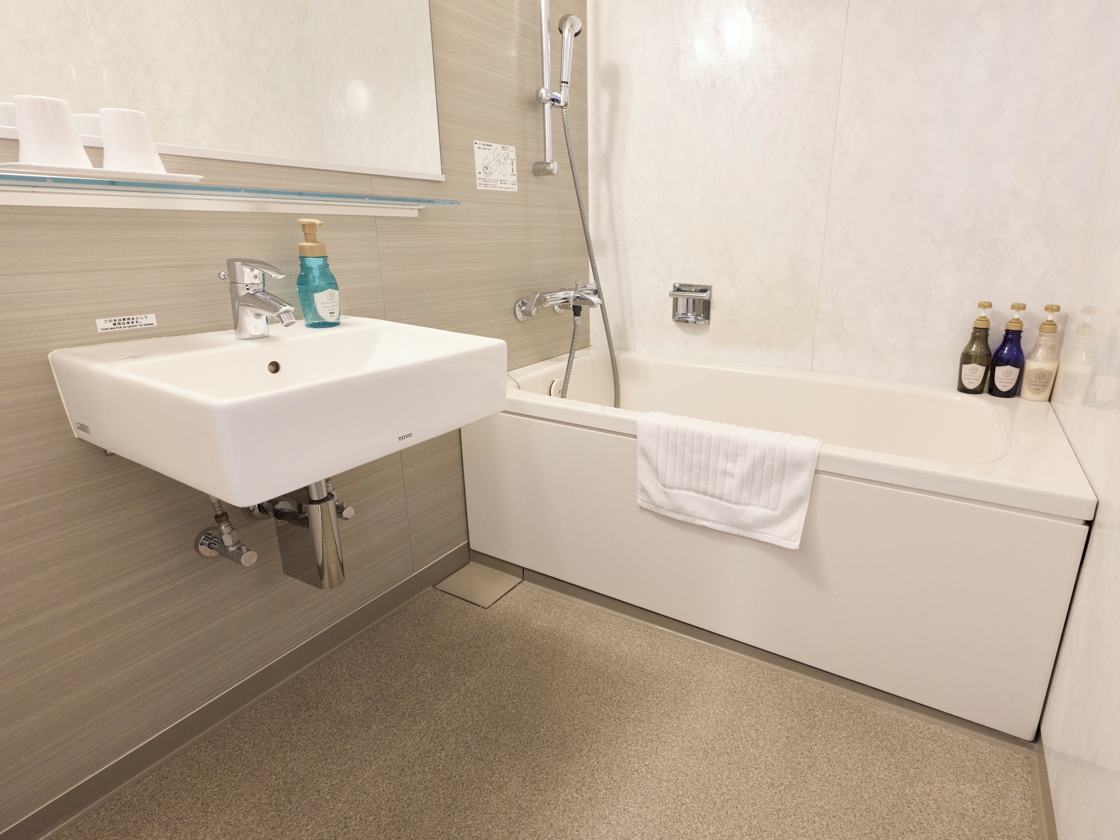 A bathroom with a white sink, a bathtub, and a glass shelf with toiletries.