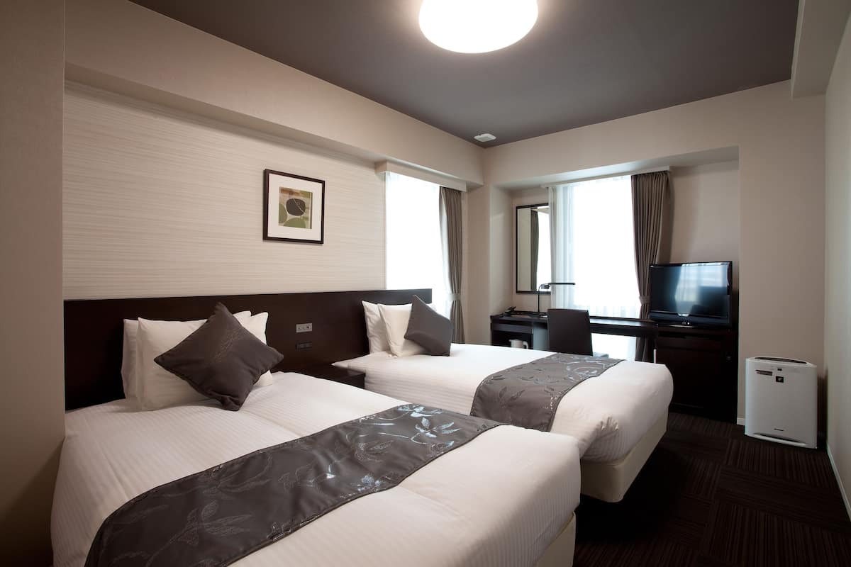 Une chambre d’hôtel avec deux lits, un bureau, une télévision et un petit climatiseur.