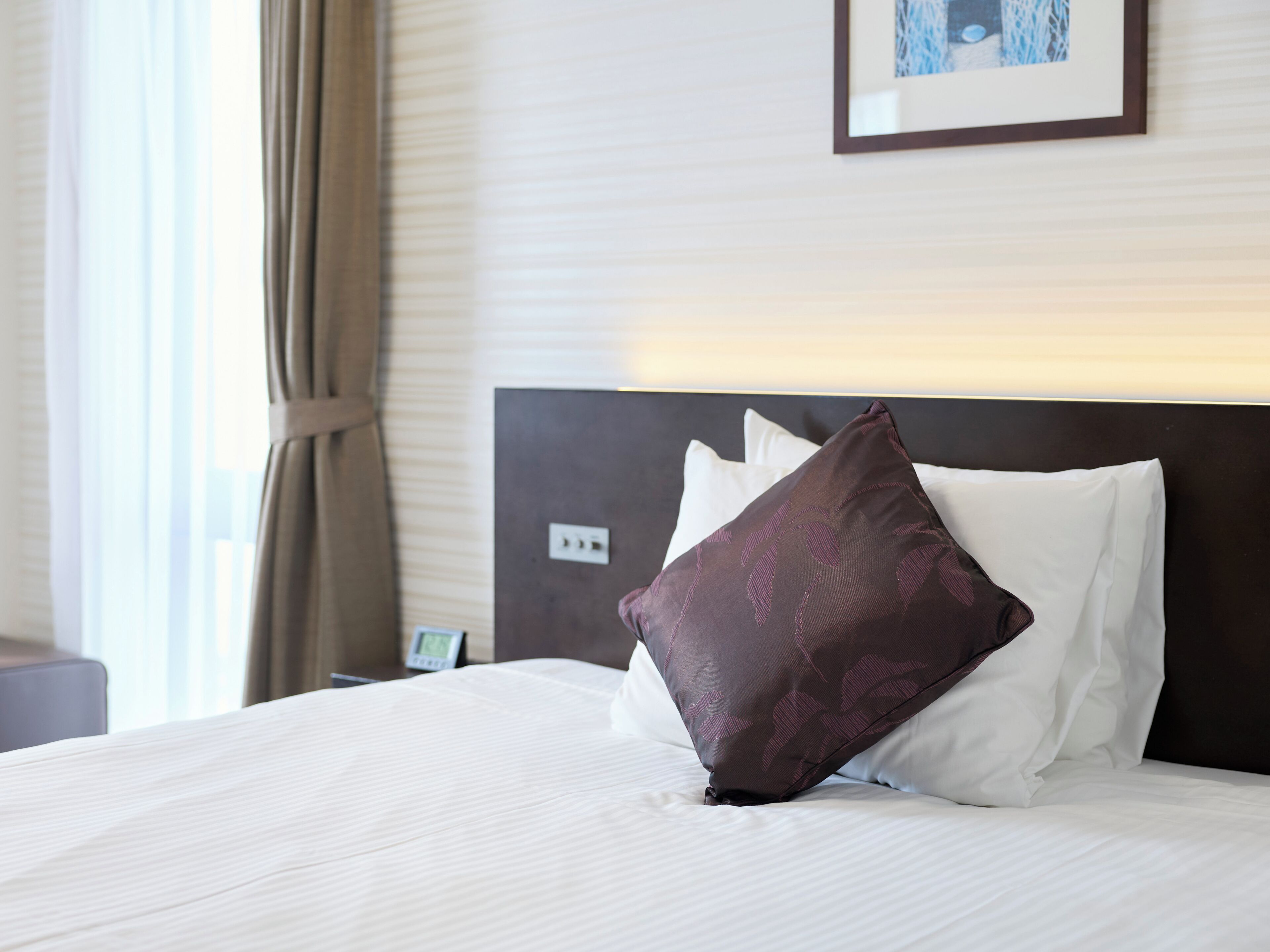 Ein Hotelzimmer mit einem aufgeräumten Bett, einem Kopfteil und einem gerahmten Bild an der Wand.