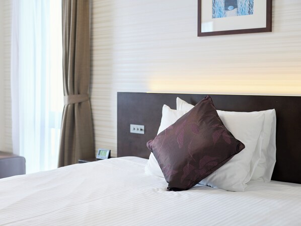 A hotel room with a neatly made bed, a headboard, and a framed picture on the wall.