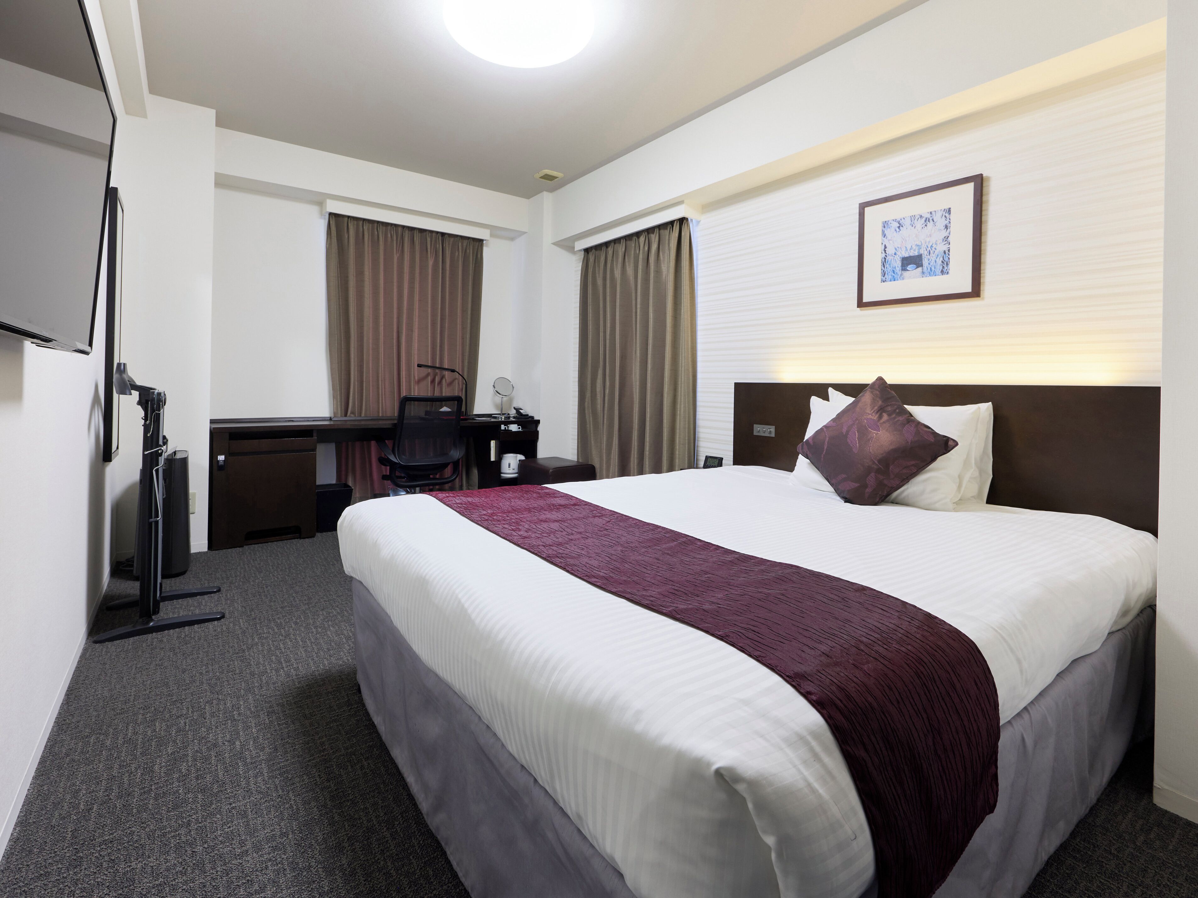 A hotel room with a large bed, a desk with a chair, a flat-screen TV, and a framed picture on the wall.