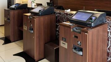 A hotel reception area with two self-service kiosks, a reception desk, and a wall-mounted sign.