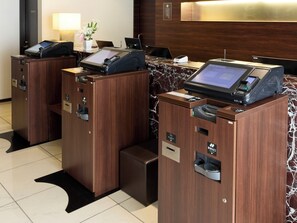 Zona de recepción de hotel con dos quioscos de autoservicio, un mostrador de recepción y un cartel en la pared.