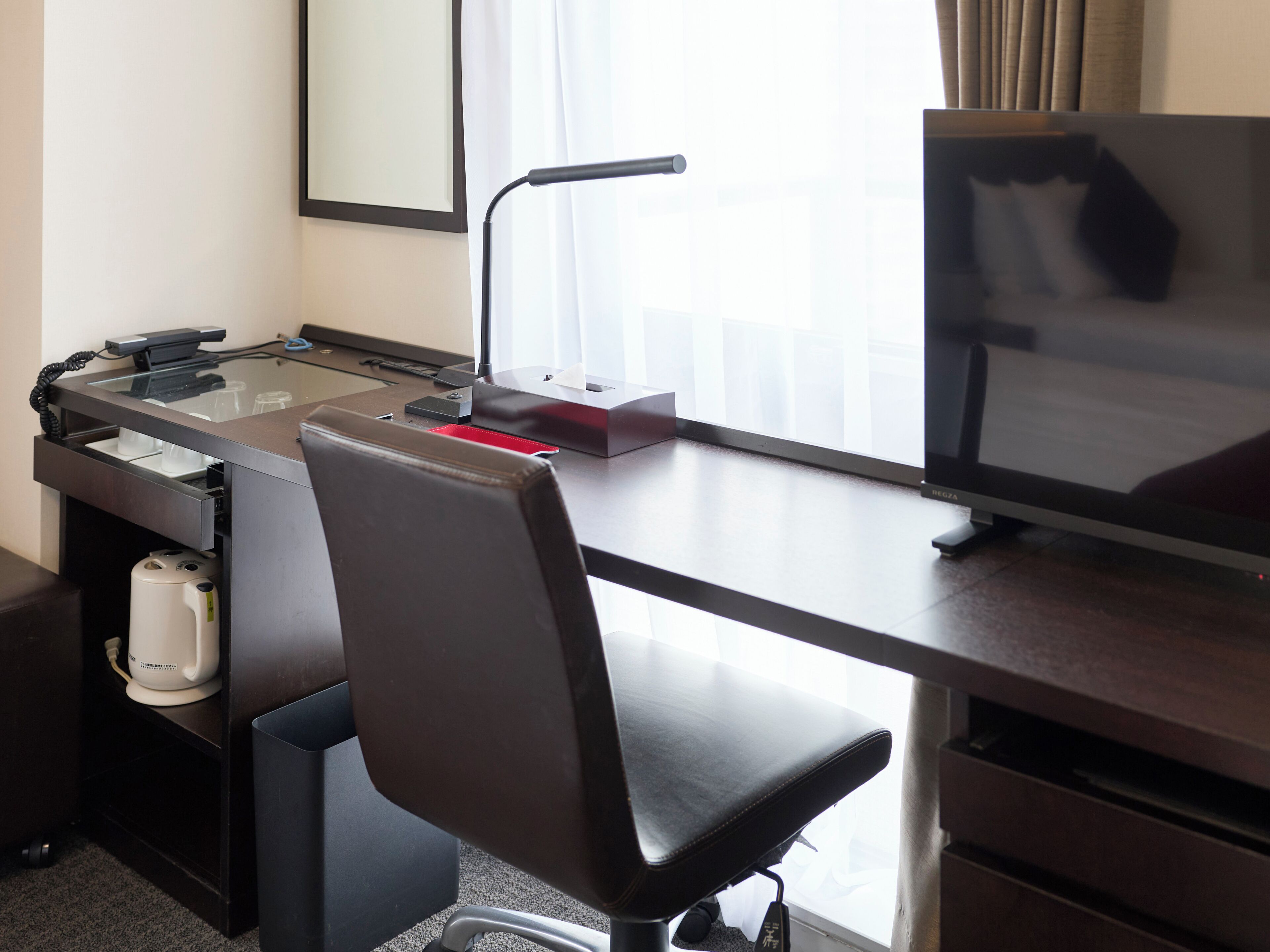 Una camera d'albergo con una scrivania, una sedia, un monitor del computer, un telefono e una macchina del caffè.