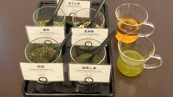 A tray with six labeled containers of tea, each with a spoon, and two cups of tea on the side.