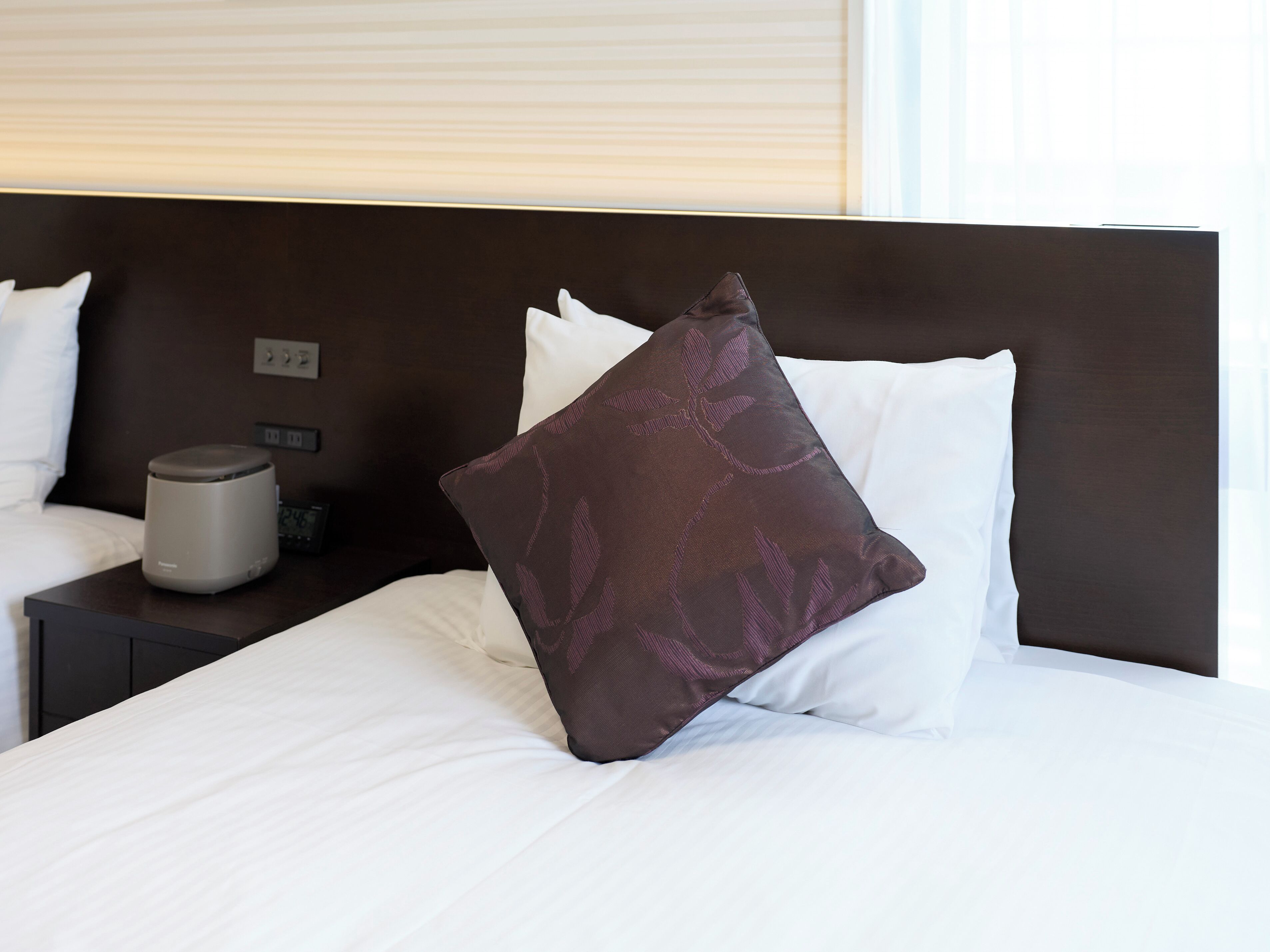 A hotel room with a neatly made bed, a bedside table with a lamp, and a power outlet.