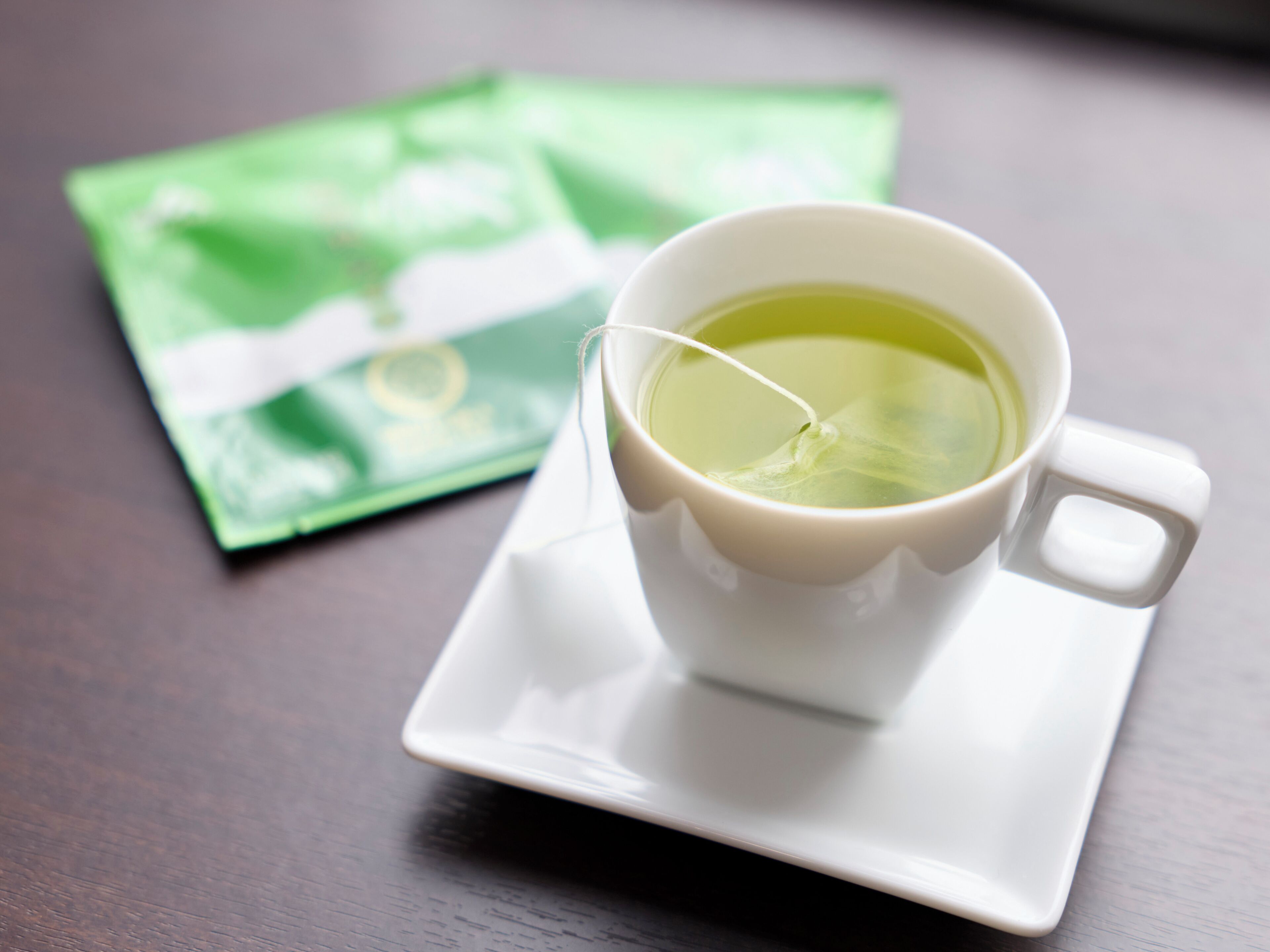 A white cup of tea on a white saucer with a green tea bag beside it.