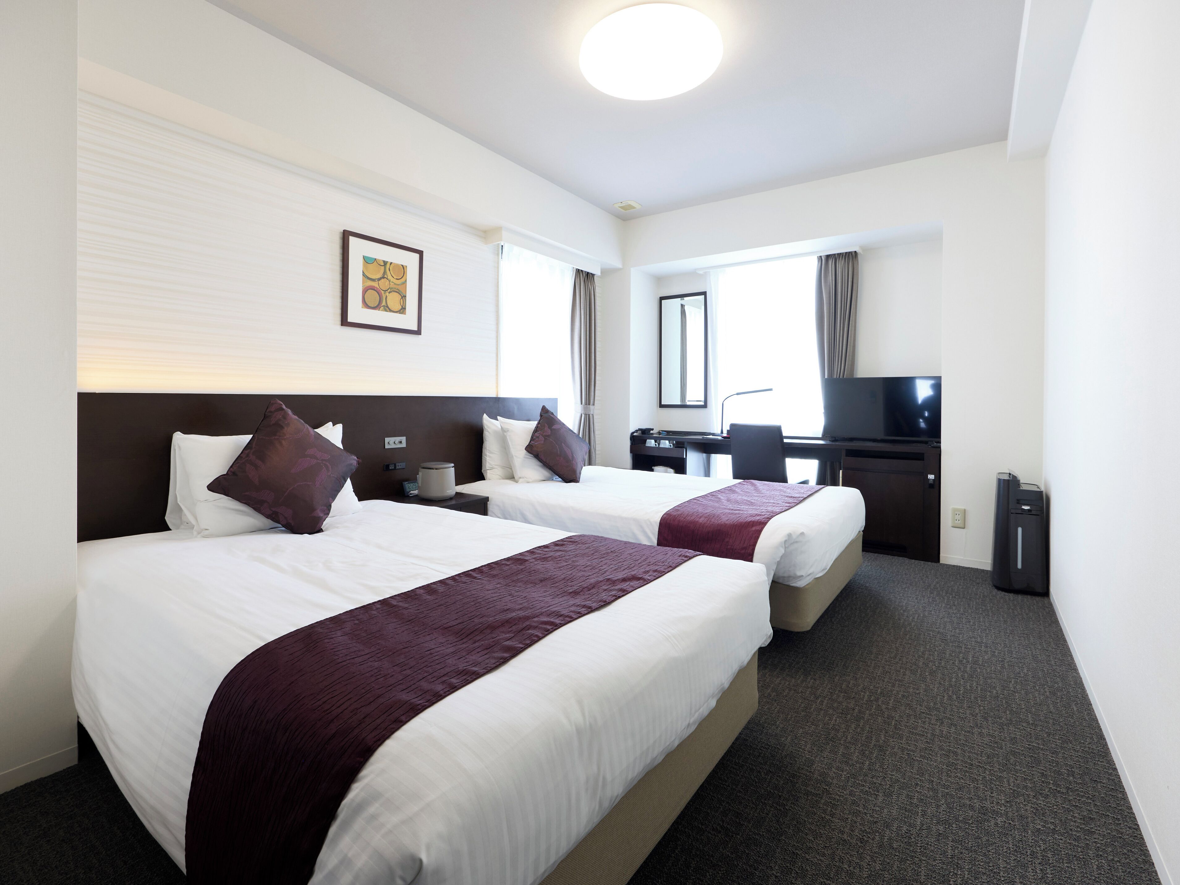 A hotel room with two beds, a desk, a television, and a window with curtains.