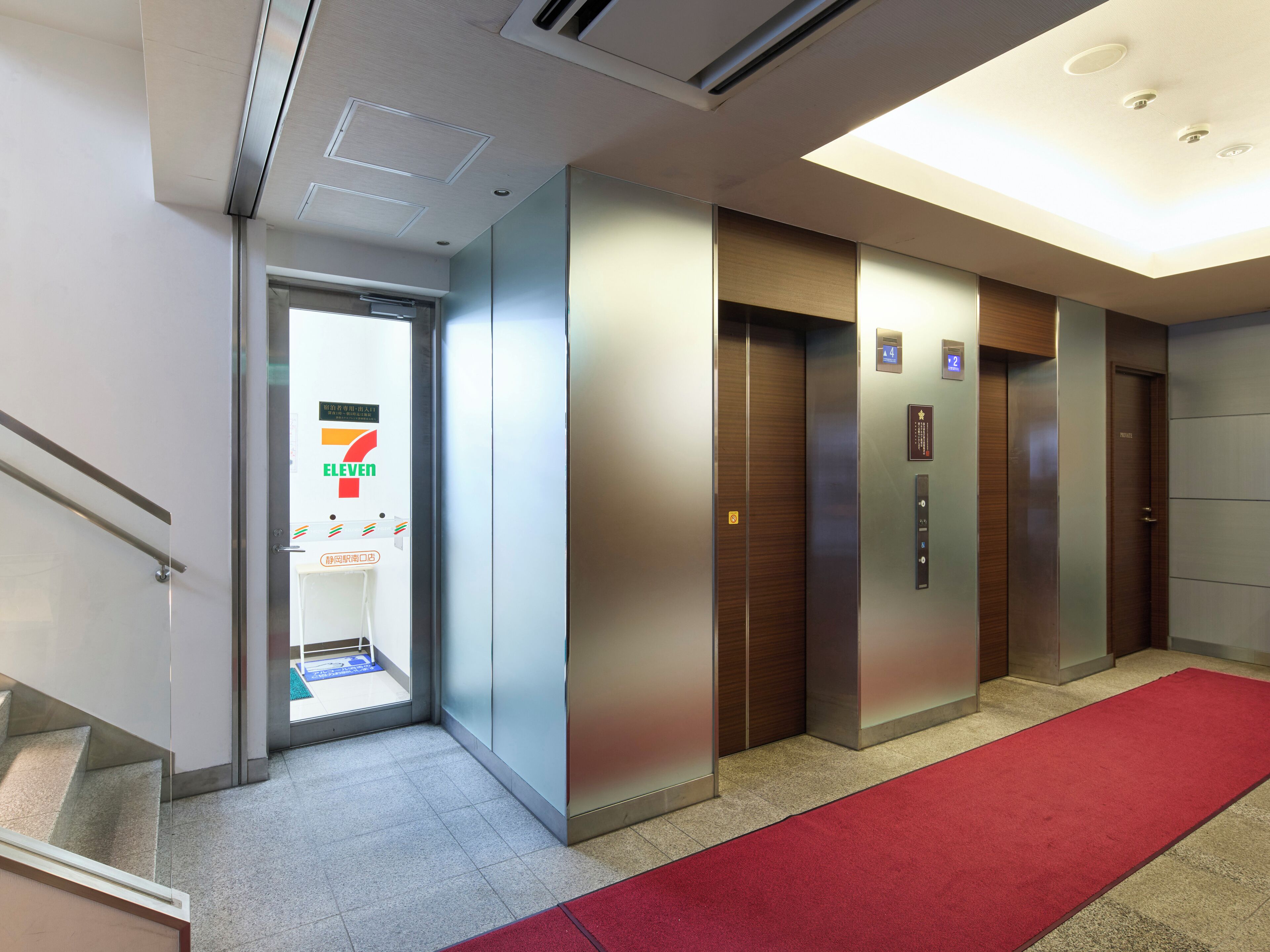 A modern elevator area with a red carpet, a 7-Eleven store, and a clear view of the elevator doors.