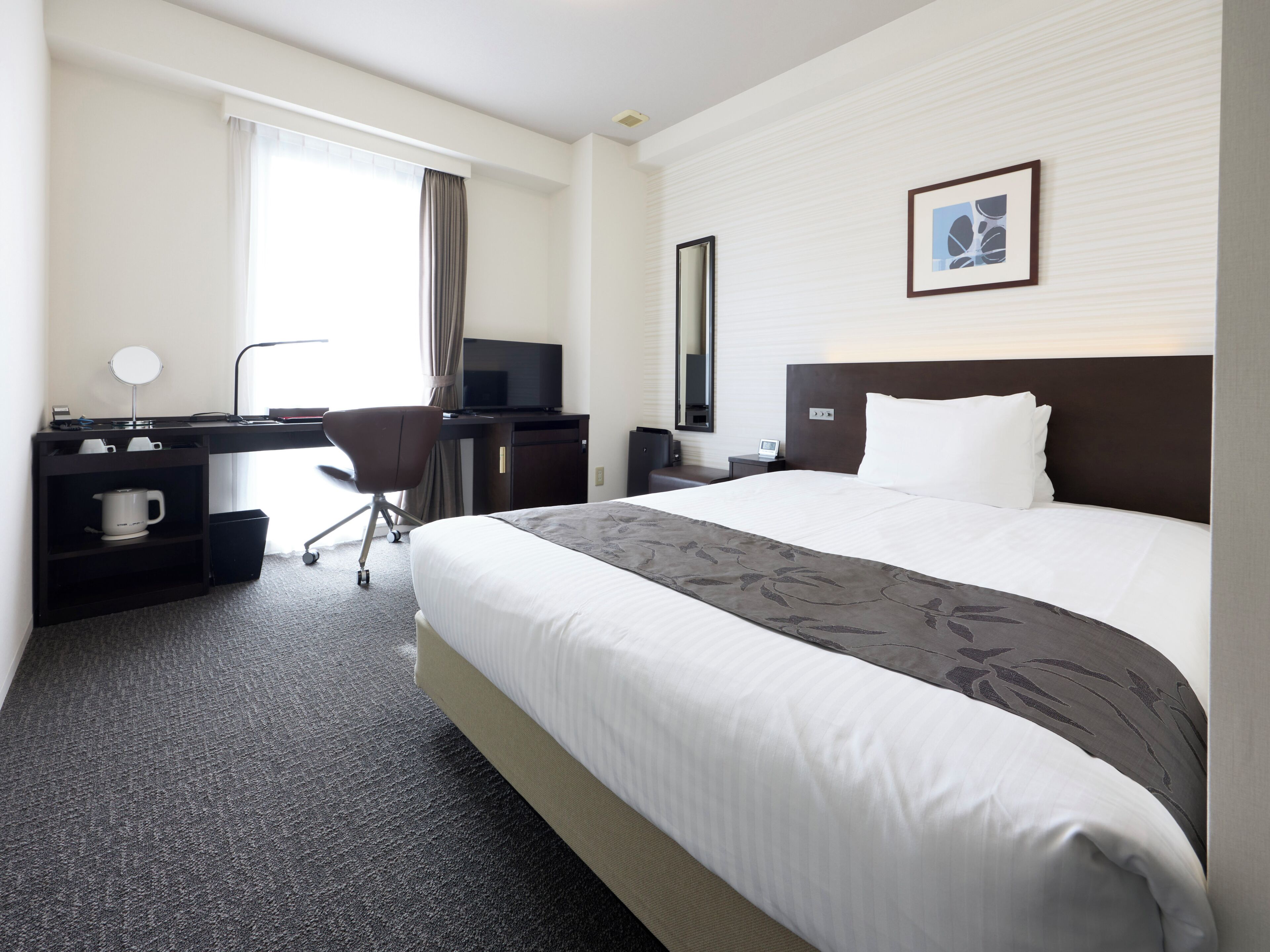 A hotel room with a bed, desk, chair, and a television.