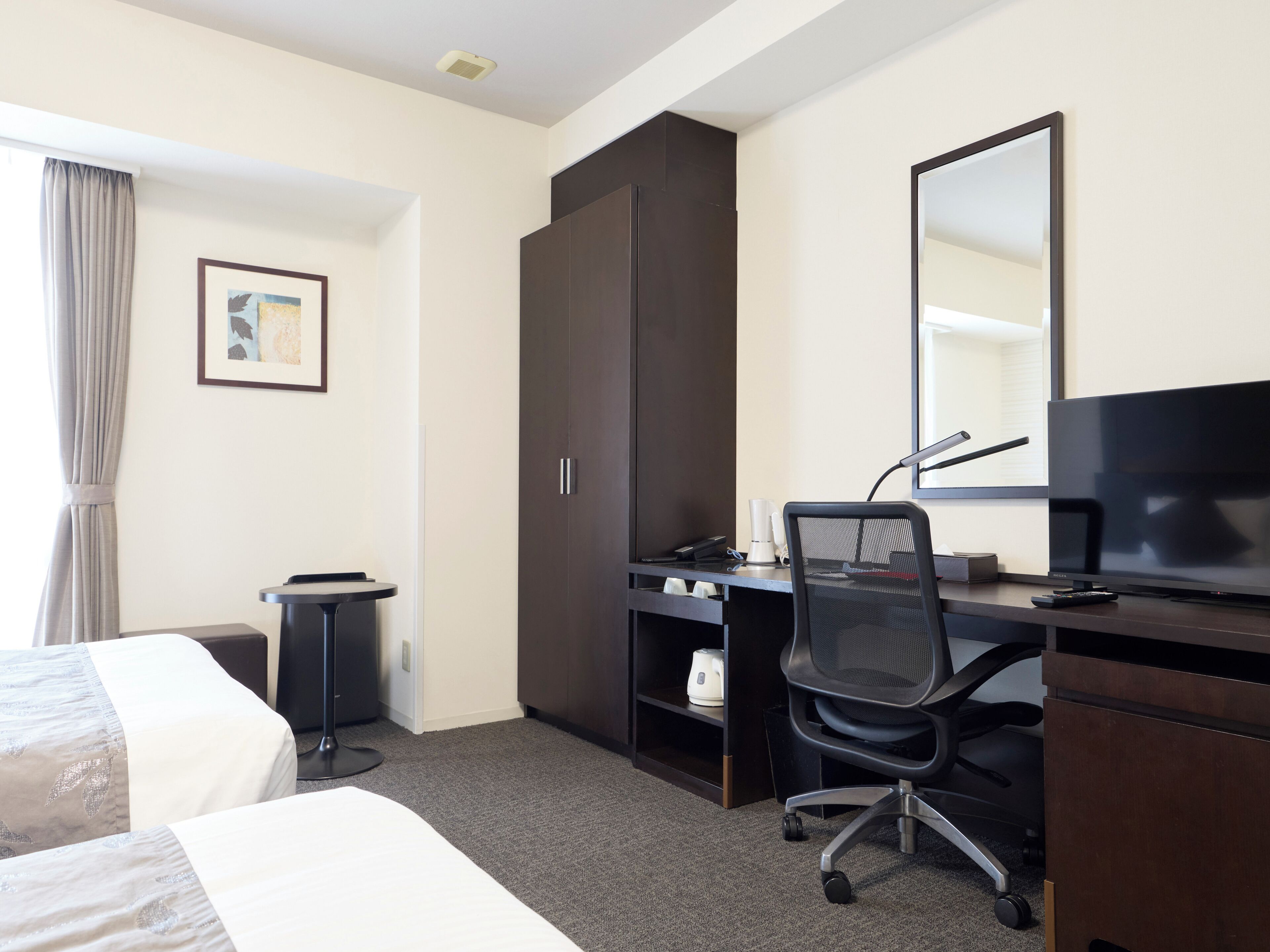 Een hotelkamer met een bed, bureau, stoel, televisie en een kledingkast.