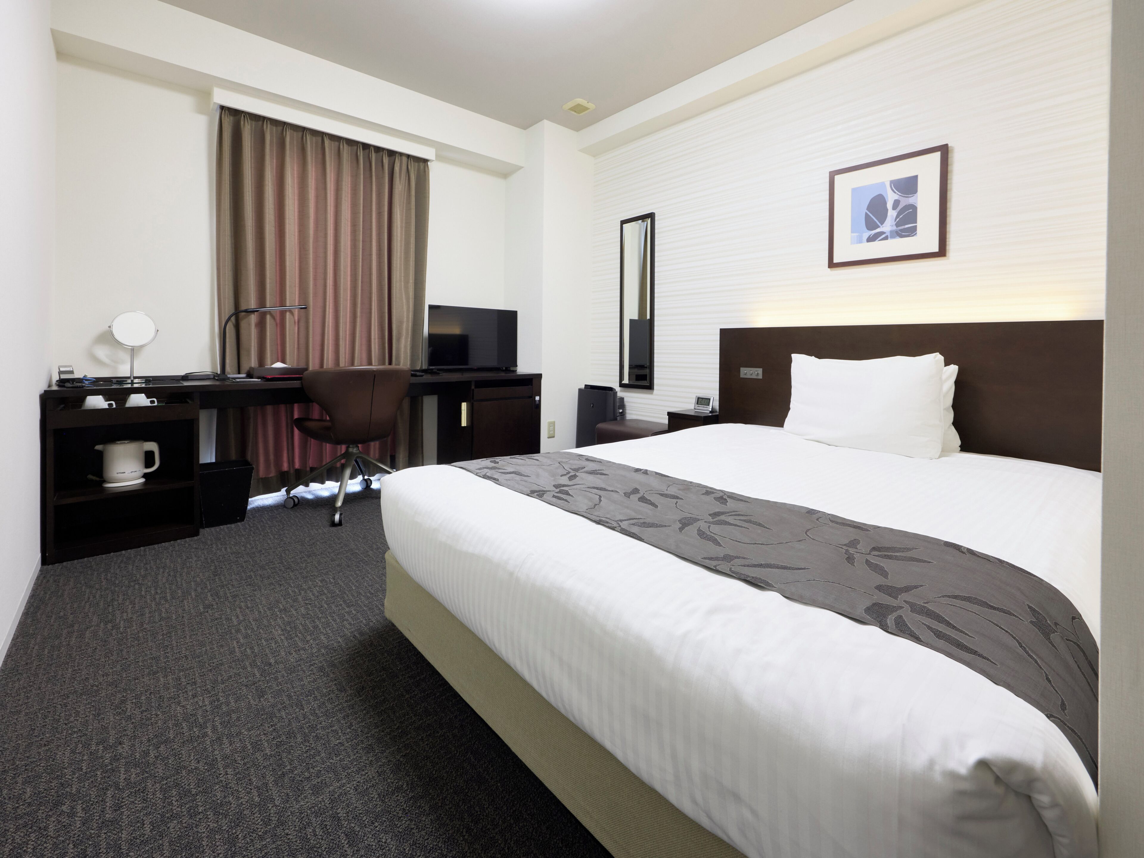 A hotel room with a bed, desk, chair, and a television.
