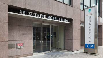 The exterior of the Shizuotetsu Hotel Prezio with a clear entrance, signage, and a parking direction sign.