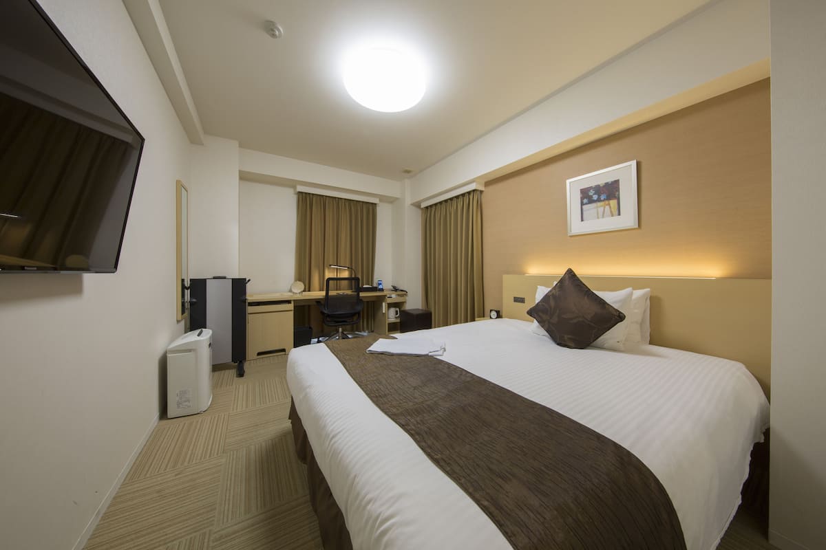 Une chambre d’hôtel avec un grand lit, un bureau, une chaise, une télévision et un tableau au mur.