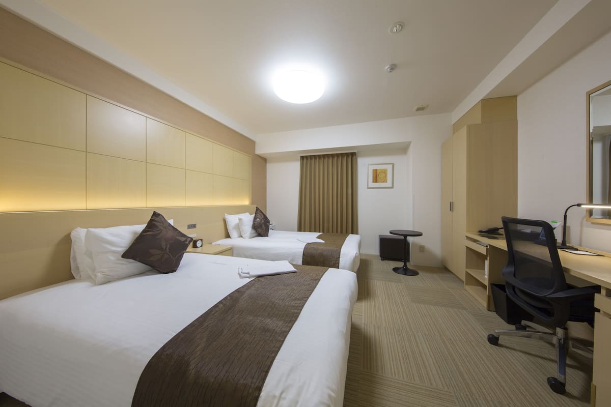 Une chambre d’hôtel avec deux lits, un bureau, une chaise et une petite table.