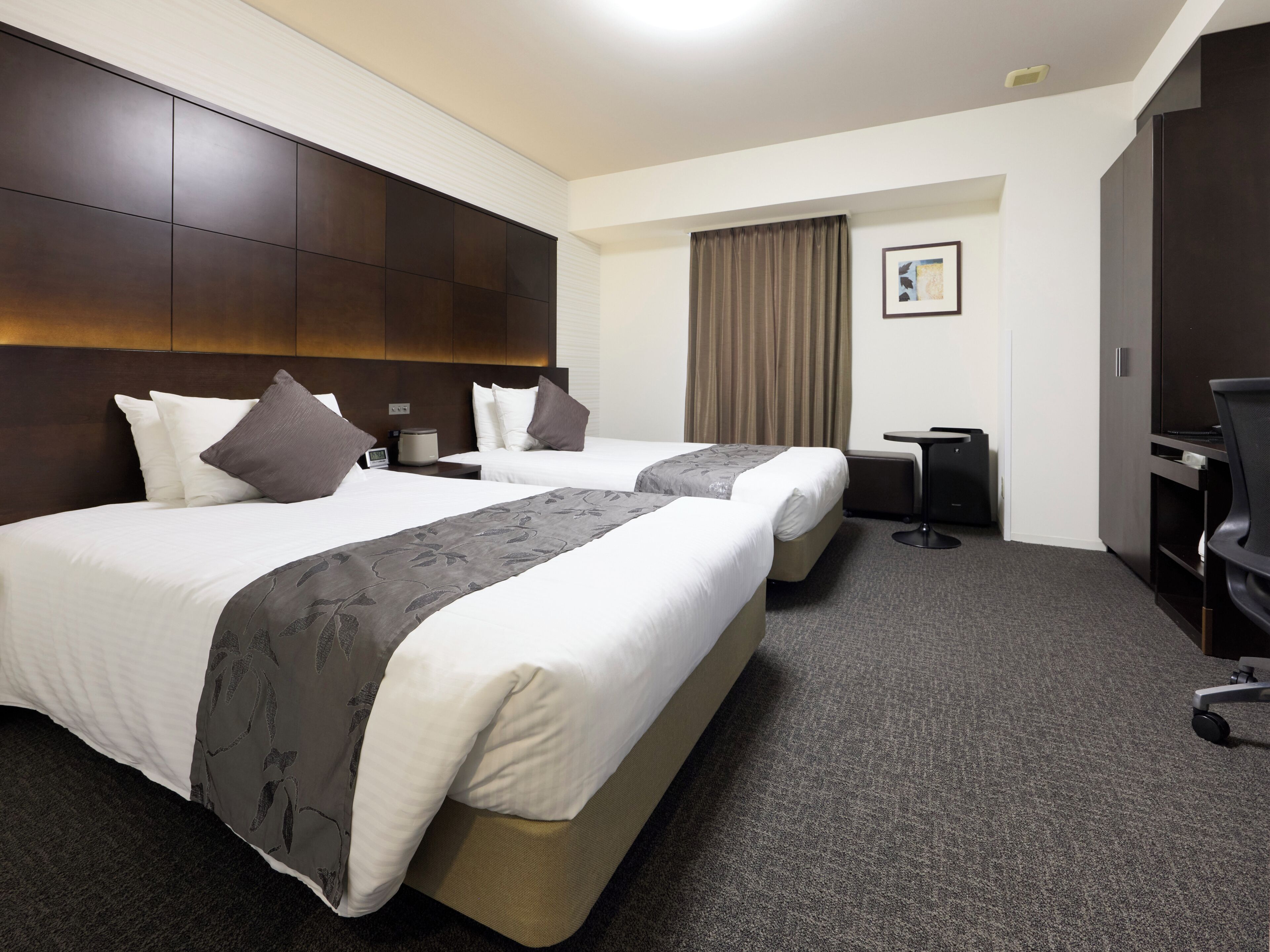A hotel room with two beds, a desk, a chair, and a television.