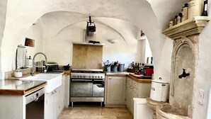 A kitchen with an arched ceiling, a stove, sink, and a stone sink.