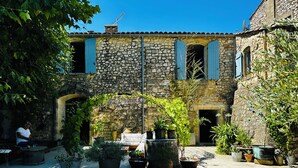 A courtyard with stone buildings, potted plants, and a person sitting on a bench.