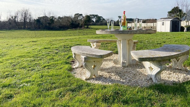 Ein Garten mit einem Steintisch und -stühlen, umgeben von einer grünen Wiese und einem kleinen Schuppen.