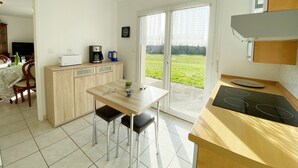 Eine Küche mit Esstisch, Stühlen, einer Kaffeemaschine und Blick auf ein grünes Feld durch die Glastür.
