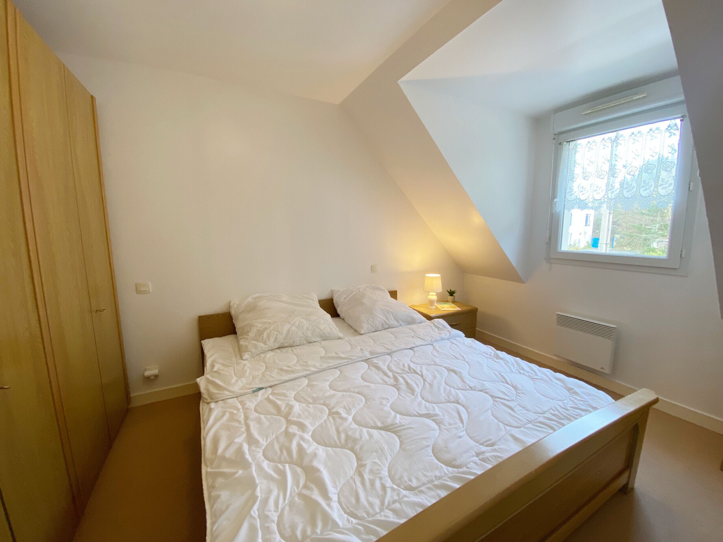 A bedroom with a bed, a nightstand, a window, and a sloped ceiling.