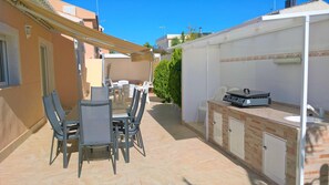 Eine Terrassengruppe im Freien mit Esstisch, Stühlen, Grill und kleinem Spülbecken.