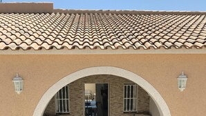 A building with a tiled roof, an arched entrance, two wicker chairs, a small table, and potted plants. - Luxury Villa south facing-Beach 500m-Private heated pool-English TV-WiFi-BBQ (SANTIAGO DE LA RIBERA)