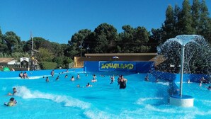 Ein Schwimmbecken mit badenden Personen, eine blaue Wand mit der Aufschrift 'AQUALAND' und einer Wasserspielfeature.