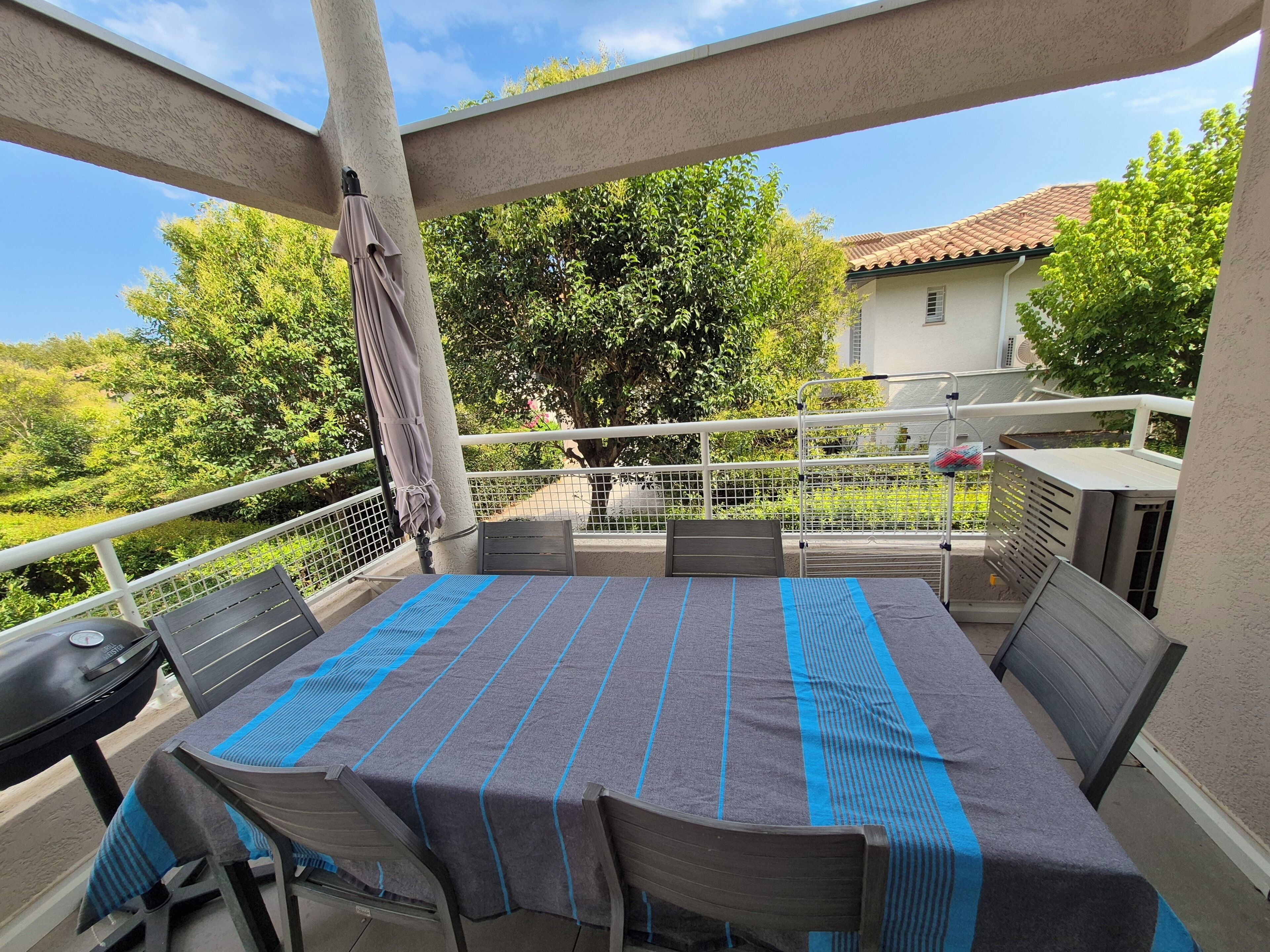 An outdoor patio with a table and chairs, a grill, and a view of a house and trees.