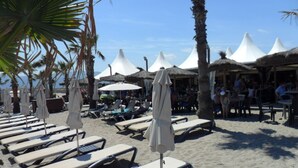 Ein Strandloungebereich mit Liegestühlen und Sonnenschirmen, Palmen und blauem Himmel.