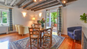 A dining area with a wooden table, chairs, and a rug. There is a sofa and a lamp in the room.
