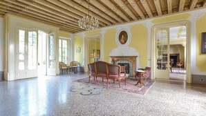 A spacious room with a high wooden ceiling, a fireplace, and a large window.