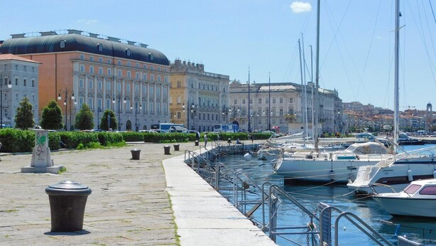 A marina with boats docked, a stone pathway, and historic buildings in the background.
