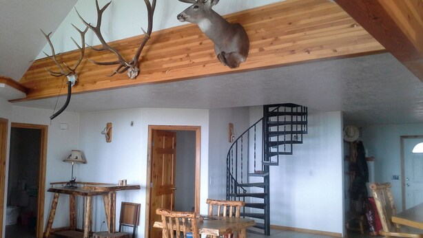 Een rustiek interieur met een houten plafond, een eethoek met houten meubels en een wenteltrap.