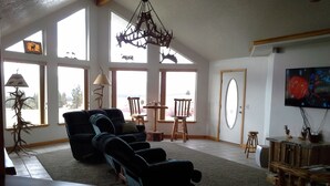 Een ruime woonkamer met een groot raam, een plafondventilator, een verstelbare fauteuil, een houten salontafel en een televisie.